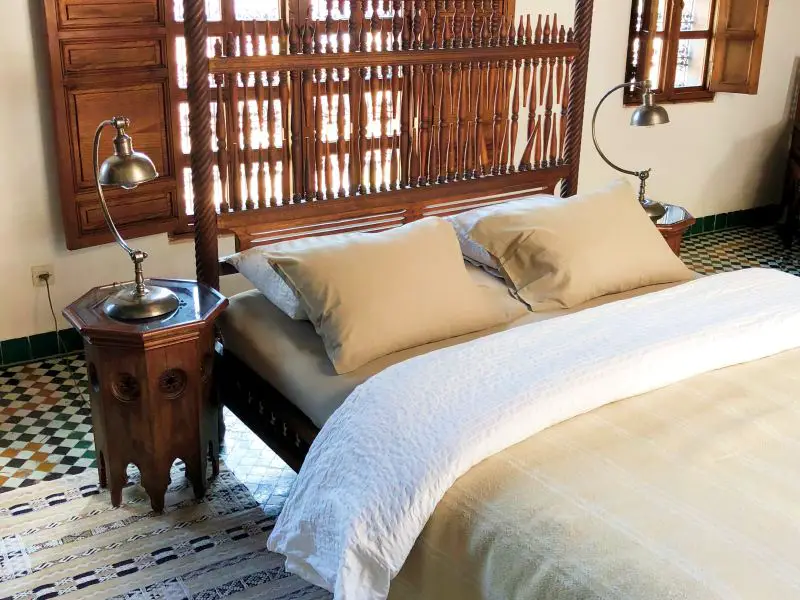 bed, wooden side table and wooden screen on window in stylish room in a riad in Morocco