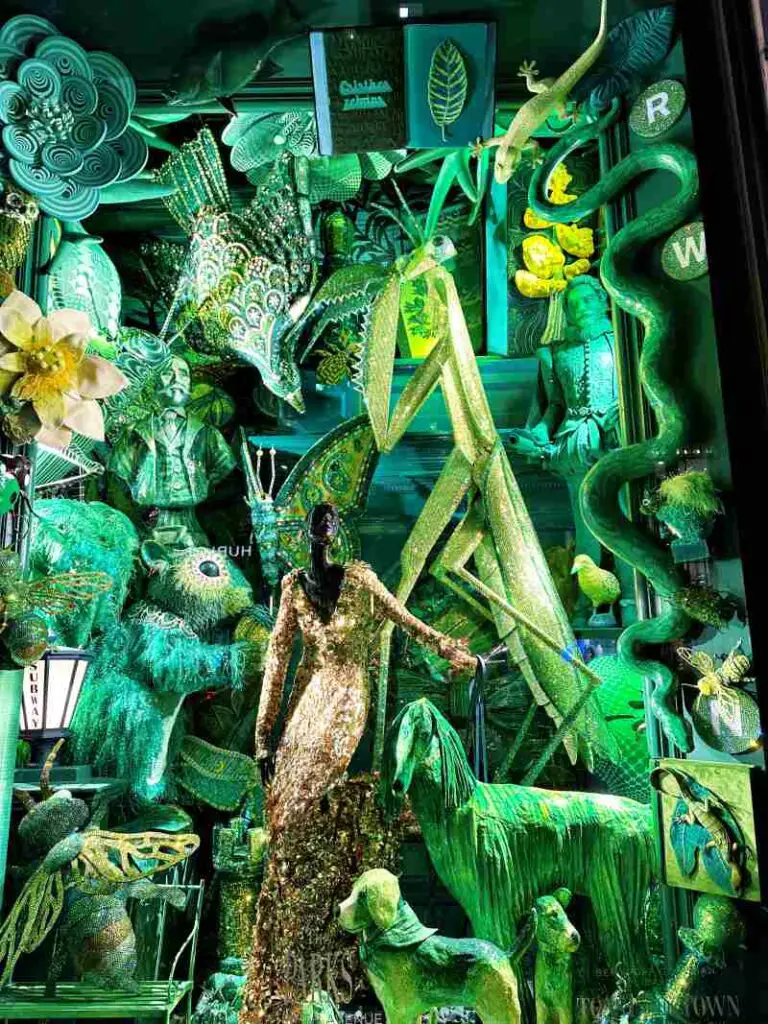 green holiday wondows with lots of fantasical inscsts and a woman mannikin dressed in s sparky gold dress