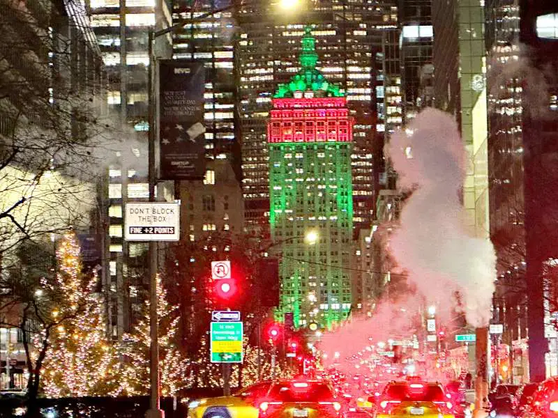 green and red skyscraper at end of street. christamas trees with lights on foreground. steam