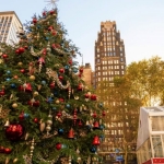 large christmas tree outsdie with a dark and gold-trimmed art deco skyscraper behind it