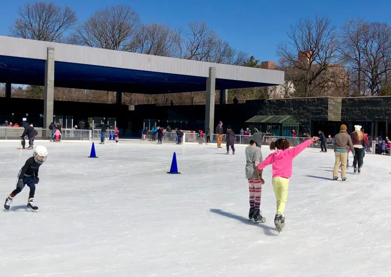 people ice skating outside with large open building nearby