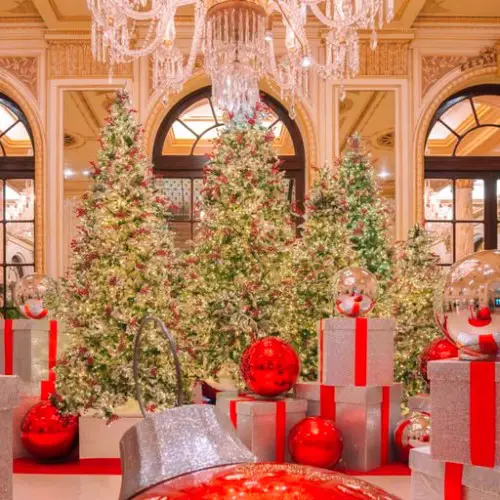 3 christmas tree and a chandelier with a large red ball in foreground